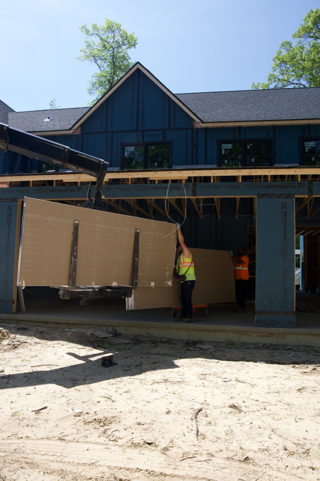 Crane lowering drywall beside the finished siding